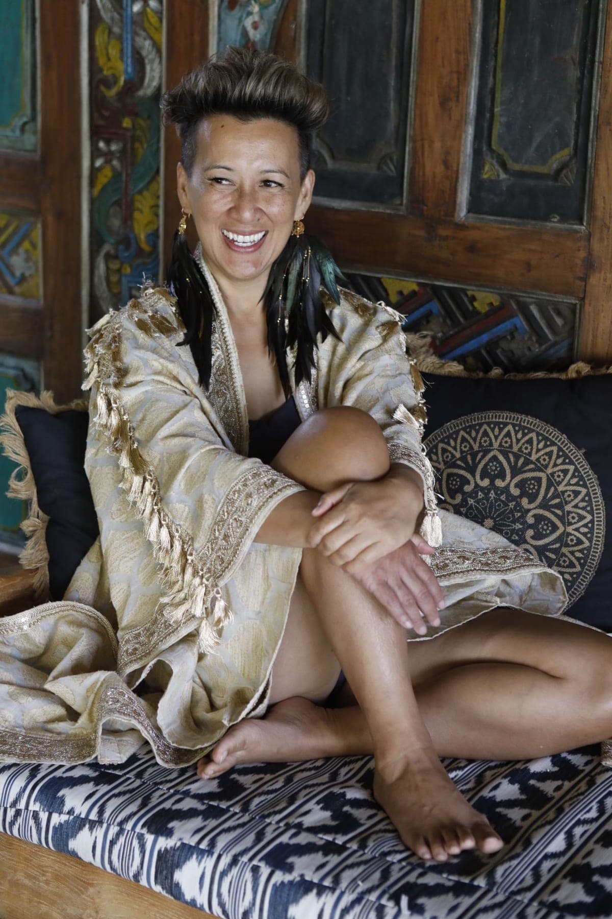 Oomee laughing on a daybed, wrapped in a gold tasselled robe