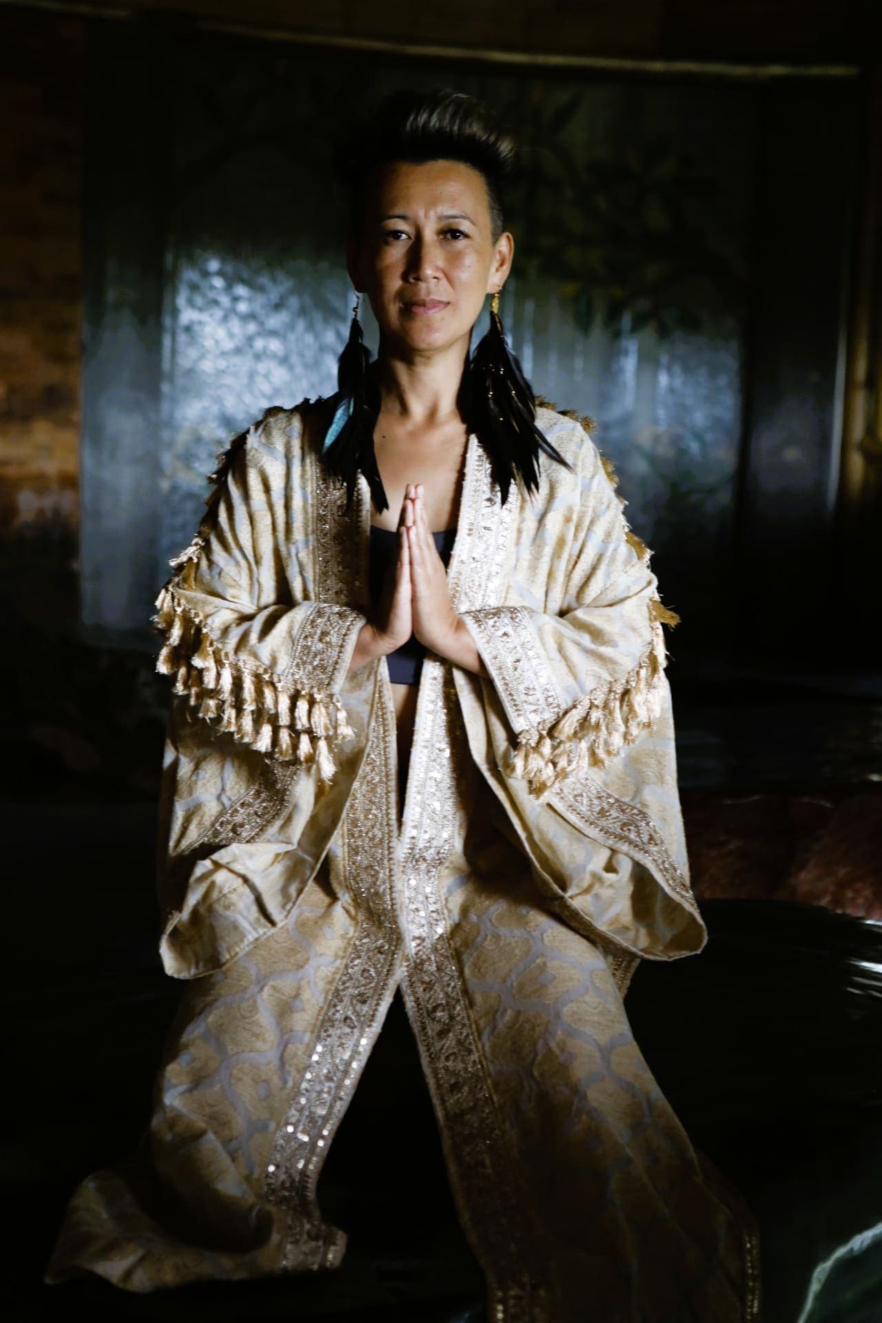 Oomee in a gold embroidered robe, hands together, looking straight at the camera