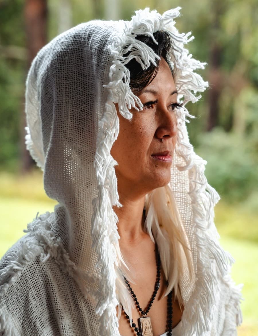 Oomee in a white fringed hood, gazing out of a window toward green forest